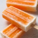 Homemade orange creamsicle popsicles on a wooden stick, ready to enjoy.