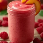 Raspberry Peach Smoothie served in a glass with fresh fruits around it