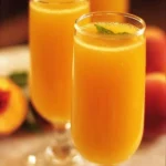 A refreshing glass of Peach Mimosas garnished with fresh peaches and mint.