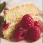 A slice of Raspberry Lemon Cake topped with fresh raspberries and lemon zest.